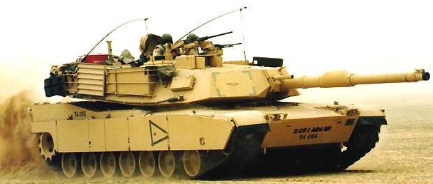 Two M1A1 Abrams tanks driving along a dusty road on an exercise in the field.