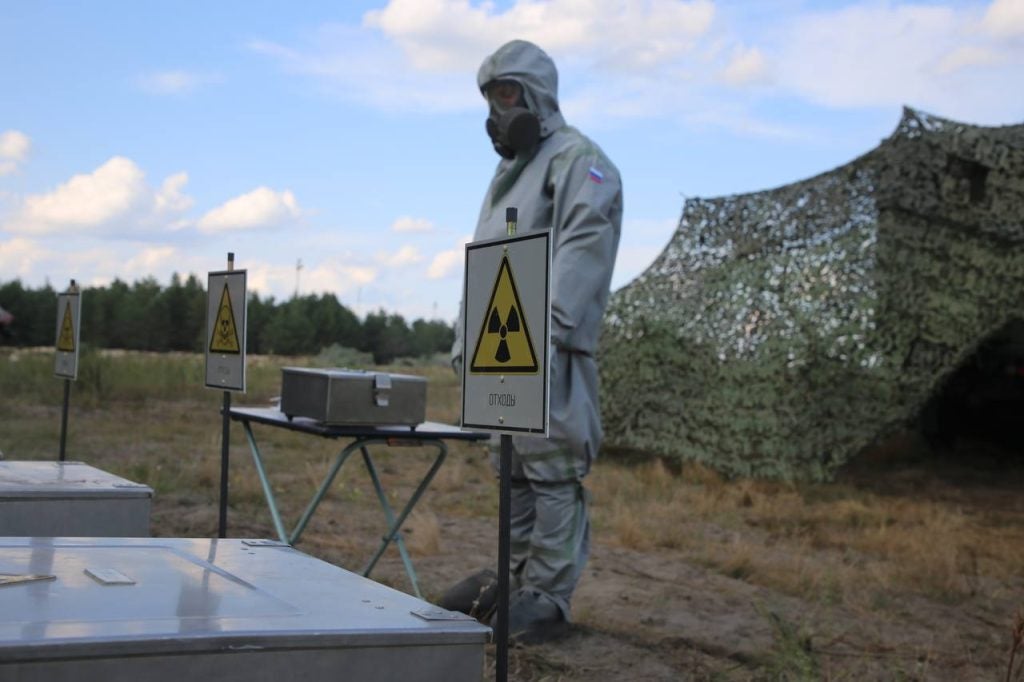 A soldier at Bretsky Training Grounds in protective clothing badged with Russian insignia standing guard over materials marked as radioactive waste, 2 September 2023. Image from the Belarusian Ministry of Defence.